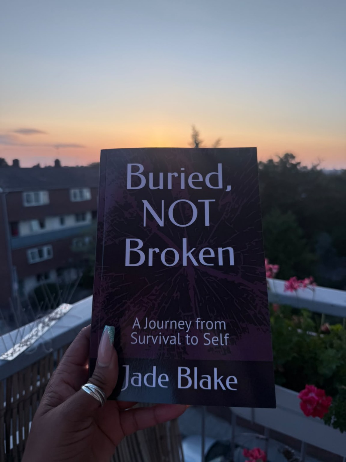 A physical copy of Buried, Not Broken by Jade Blake held against a sunset